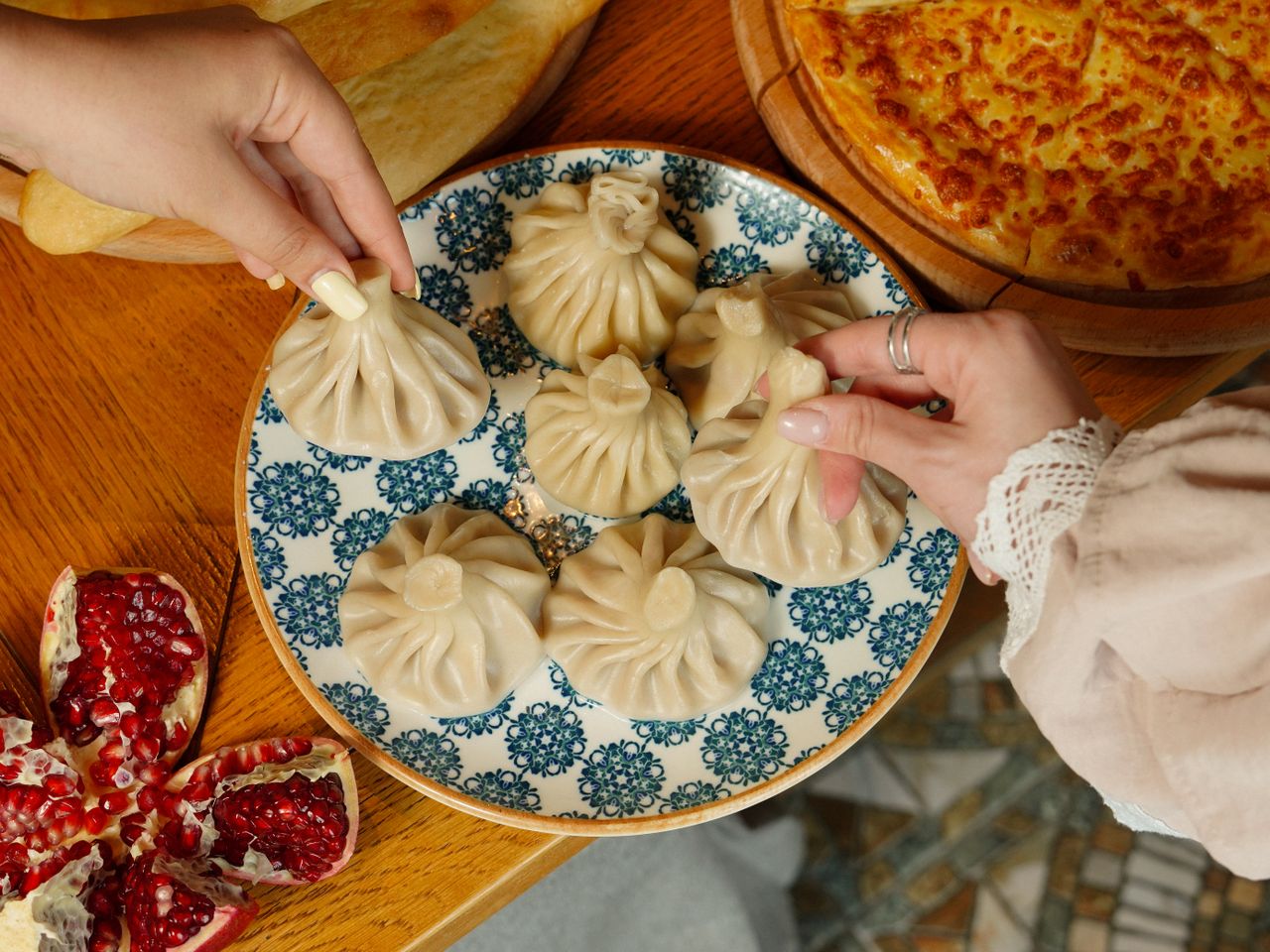 Nahaufnahme von georgischen Teigtaschen Khinkali mit Brot und Granatapfel auf einem Holztisch.