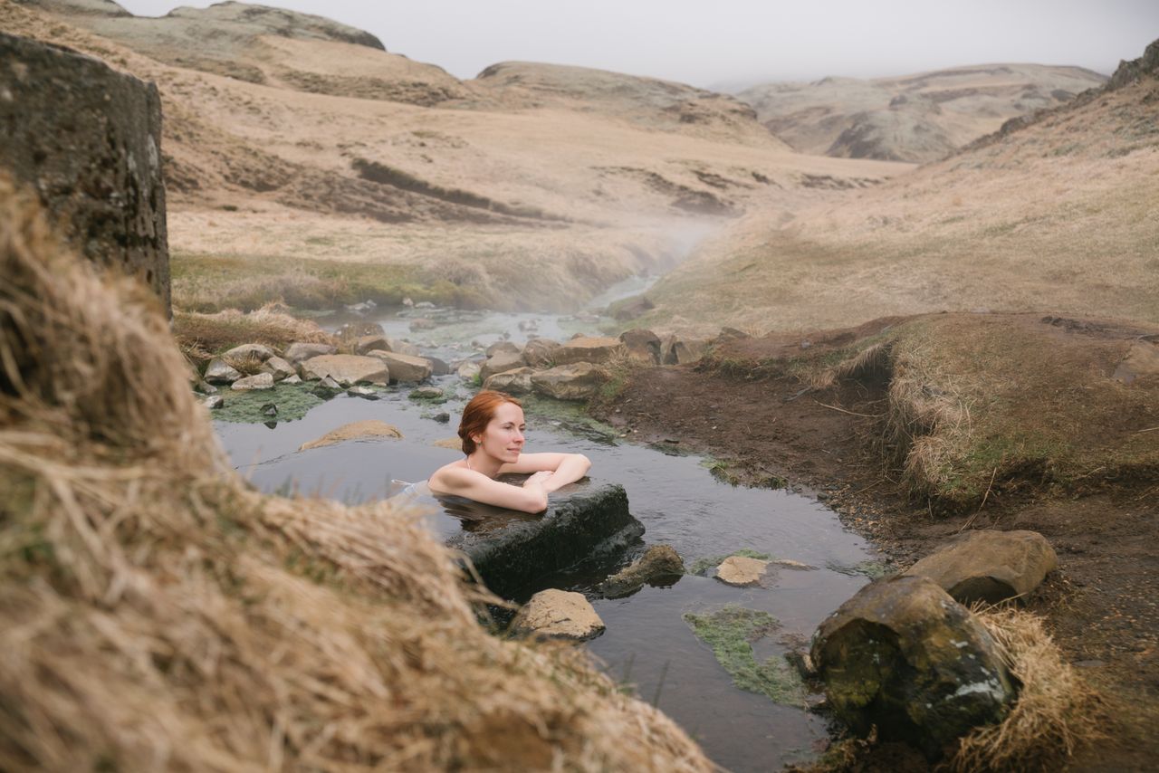Eine friedliche Szene einer Frau, die eine natürliche heißen Quelle in einer ruhigen hügeligen Landschaft genießt.